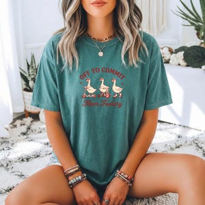 Könnte beinhalten: Ein kurzärmeliges T-Shirt in Blaugrün mit einer Grafik von drei Gänsen in roter Farbe. Der Text "OFF TO COMMIT" steht über den Gänsen und "Mom Foolery" darunter. Die Gänse sind auf einem Roller, einem Fahrrad und mit Rollschuhen abgebildet.