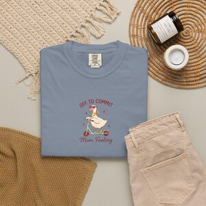 Könnte beinhalten: Ein schieferblaues T-Shirt mit Rundhalsausschnitt und einer Stickerei einer weißen Ente, die herzförmige Sonnenbrillen und ein gelbes Halstuch trägt und auf einem türkisfarbenen Roller fährt. Der Text lautet OFF TO COMMIT Mom Foolery in Kastanienbraun.