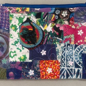 May include: A patchwork zippered pouch with a blue zipper and trim. The pouch is made of various fabric squares in shades of purple, blue, green, and orange. Some squares feature floral and frog patterns, and a circular patch with a black bird.