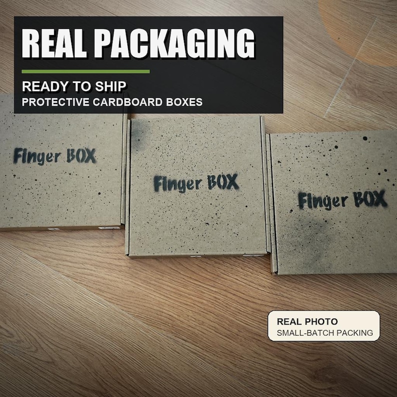 May include: Three square cardboard boxes with a speckled grey finish, each featuring the text Finger BOX in black stencil-style lettering. The boxes are arranged in a row, showcasing protective packaging for shipping small items.