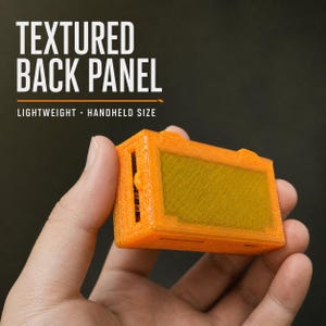 May include: A bright orange rectangular handheld device featuring a textured back panel. The text "TEXTURED BACK PANEL" and "LIGHTWEIGHT - HANDHELD SIZE" is printed in white above the object. The device has a central recessed rectangular area.