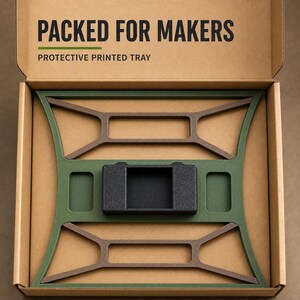 May include: A cardboard box labelled PACKED FOR MAKERS PROTECTIVE PRINTED TRAY containing a green and brown geometric frame with a central black rectangular component. The frame features symmetrical cutouts and a textured finish within the box.