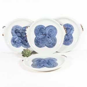 May include: Set of three white ceramic plates with blue and brown swirl designs. Each plate has a small handle on the side.