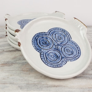 May include: A set of four white ceramic plates with blue and brown designs. The plates have a scalloped edge and a unique design in the center.