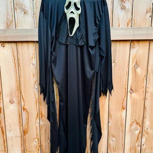 May include: A black hooded robe featuring long, jagged-edged sleeves and a white, elongated ghost mask with hollow black eye sockets and an open mouth. The costume is constructed from a smooth, lightweight fabric and includes an attached hood.