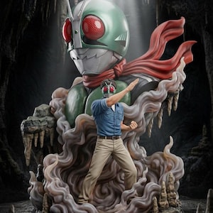 Puede incluir: Estatua detallada de un superhéroe enmascarado con un gran casco verde y ojos rojos, que lleva una bufanda roja. Una figura más pequeña con camisa azul y pantalones color beige está en pose de lucha, rodeada de un efecto de humo. El fondo es una cueva.