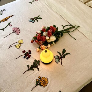 K&ouml;nnte beinhalten: Cremefarbenes Bettw&auml;sche-Set mit gestickten Blumenakzenten. Ein Strau&szlig; Rosen in verschiedenen Farben liegt auf dem Bett, neben einer kleinen, gelben Lampe. Die Bettw&auml;sche umfasst ein Bettlaken, ein Spannbetttuch und Kissenbez&uuml;ge.