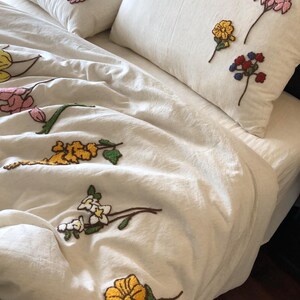 K&ouml;nnte beinhalten: Cremefarbenes Bettw&auml;sche-Set mit gestickten Blumenmustern in Gelb, Rosa, Rot und Wei&szlig;. Das Set beinhaltet einen Bettbezug und zwei Kissenbez&uuml;ge. Die Blumen sind mit einem strukturierten, erhabenen Effekt gestickt, der dem Stoff Tiefe verleiht.