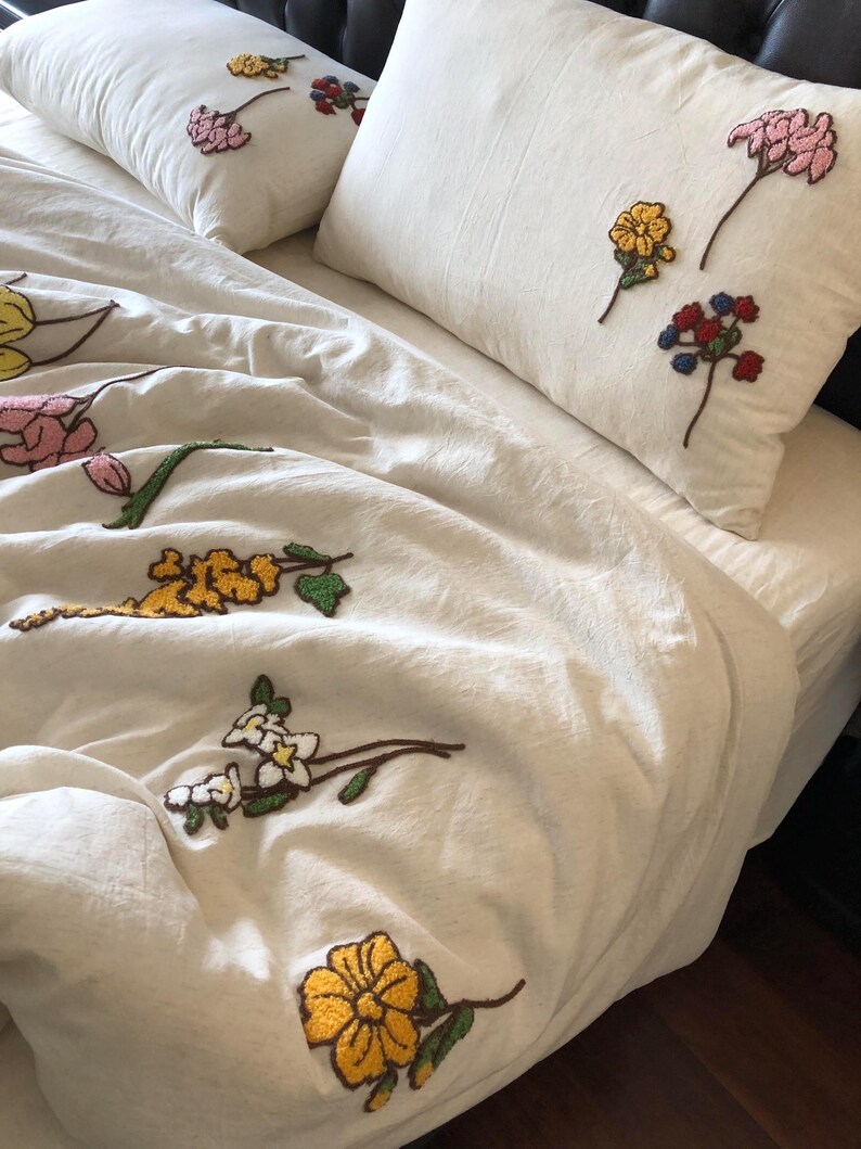 K&ouml;nnte beinhalten: Cremefarbenes Bettw&auml;sche-Set mit gestickten Blumenmustern in Gelb, Rosa, Rot und Wei&szlig;. Das Set beinhaltet einen Bettbezug und zwei Kissenbez&uuml;ge. Die Blumen sind mit einem strukturierten, erhabenen Effekt gestickt, der dem Stoff Tiefe verleiht.