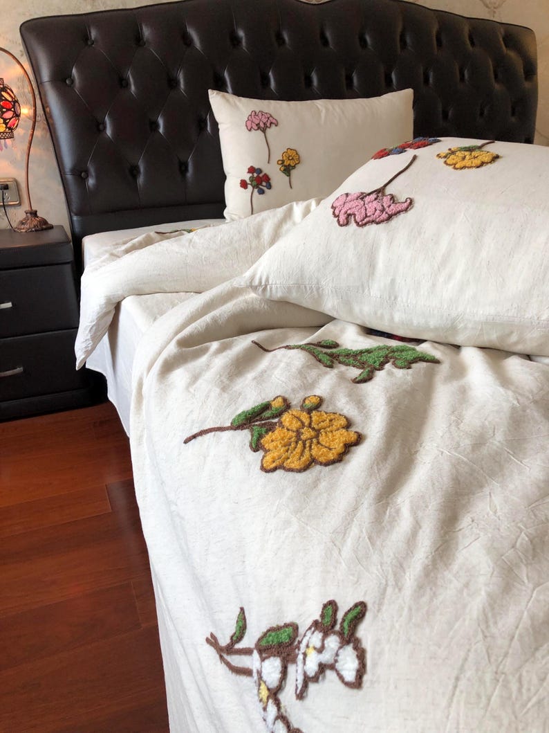 K&ouml;nnte beinhalten: Cremefarbenes Bettw&auml;sche-Set mit gestickten Blumendesigns in Rosa, Gelb und Gr&uuml;n. Das Set beinhaltet einen Bettbezug und Kissenbez&uuml;ge. Das Bett hat ein dunkelbraunes, getuftetes Kopfteil.