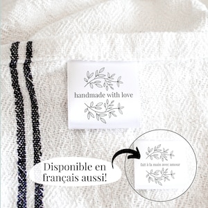 May include: White fabric with black stripes and a white label that says "handmade with love" with a floral design. The label is attached to the fabric with a white thread. The fabric is folded in half and the label is visible on the outside of the fold. There is a white circle with a floral design and the text "fait à la main avec amour" in black text.
