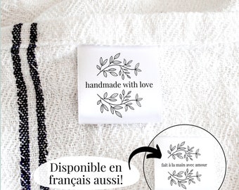May include: White fabric with black stripes and a white label that says "handmade with love" with a floral design. The label is attached to the fabric with a white thread. The fabric is folded in half and the label is visible on the outside of the fold. There is a white circle with a floral design and the text "fait à la main avec amour" in black text.