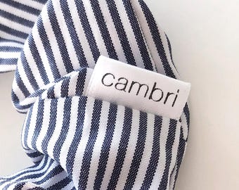 May include: A white fabric scrunchie with blue stripes and a white label that says "cambri".