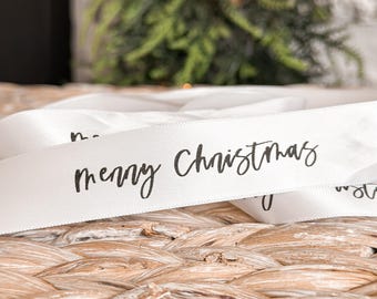 May include: White satin ribbon with the text "merry Christmas" written in black cursive.