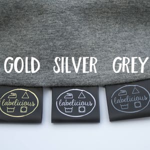 May include: Three black fabric labels with the words "labelicious" printed in gold, silver, and grey. The labels are attached to a grey fabric background with the words "GOLD", "SILVER", and "GREY" printed in white.
