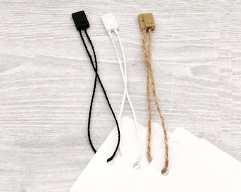 May include: Three different types of string tags with plastic tips. The tags are black, white, and brown. The tags are attached to white paper.