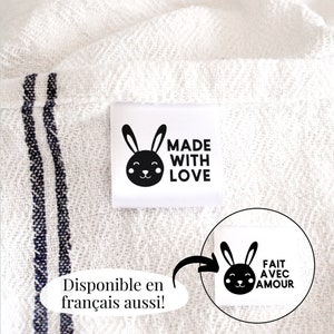 May include: White fabric with a black and white label that says "Made with Love" and features a cartoon bunny. The label is attached to the fabric with a white thread. The fabric has two black stripes running horizontally across it.