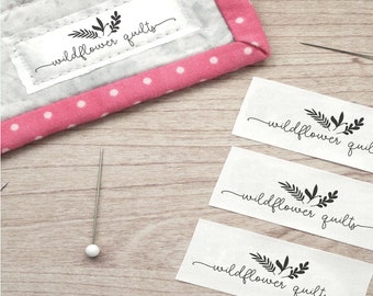 May include: Three white fabric labels with black ink, each featuring a simple floral design and the text "wildflower quilts".