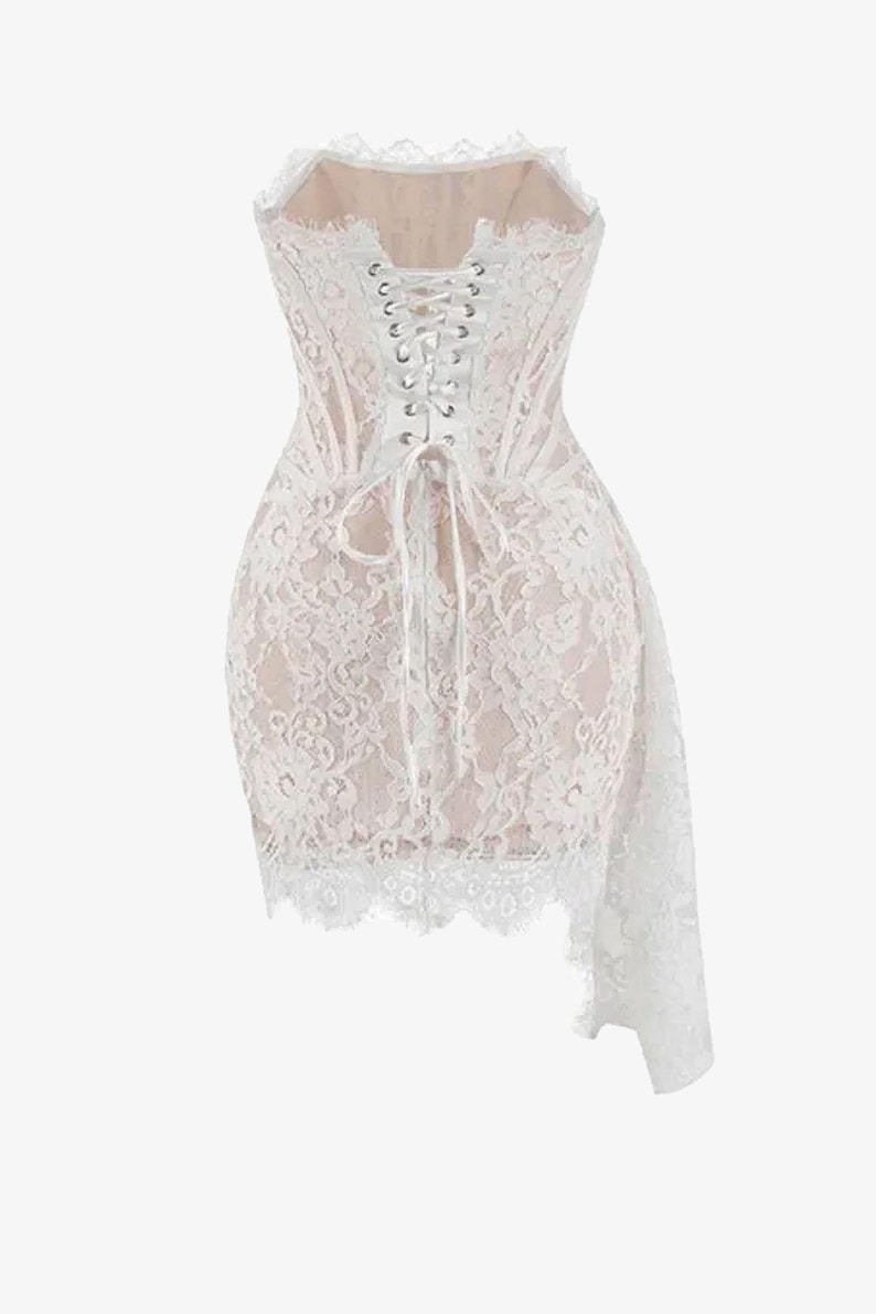 May include: A white lace corset dress with a sweetheart neckline and a lace-up back. The dress features a fitted bodice and a short skirt with a flowing, asymmetrical lace overlay. The dress is a delicate and romantic piece.