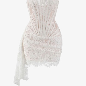May include: A white lace dress with a strapless, corset-style bodice. The dress features a draped skirt and a delicate lace trim along the neckline and hem. The dress is a formal wear item.