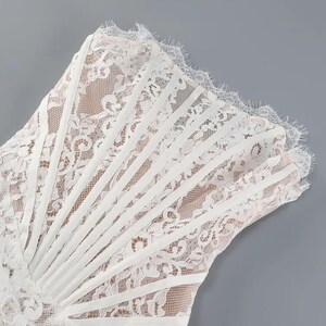 May include: White lace dress with a detailed floral pattern. The dress features a strapless design with vertical satin ribbon accents and a scalloped lace trim. The dress is set against a gray background.