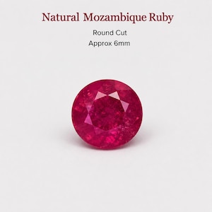 May include: A round cut natural Mozambique ruby gemstone with a deep red colour. The text above the stone reads Natural Mozambique Ruby, Round Cut, Approx 6mm. The gemstone features a faceted surface that reflects light across its circular shape.