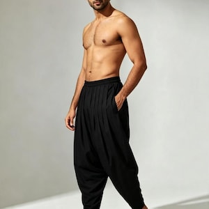 May include: Solid black harem trousers featuring a high-waisted design with a gathered elastic waistband, deep vertical pleats extending from the waist, side pockets, and a tapered leg silhouette that narrows towards the ankle for a relaxed fit.