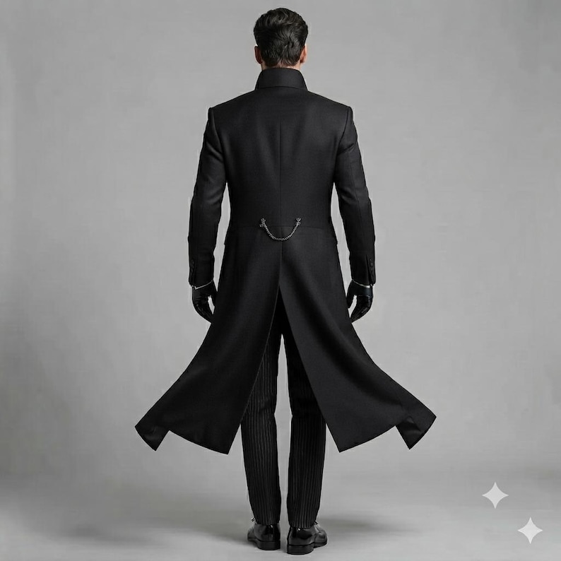 May include: A long black coat with a high collar and long sleeves, featuring a silver chain detail across the back waist. The coat is worn over dark pinstriped trousers and paired with black gloves, shown from a rear-facing perspective.