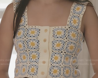 Puede incluir: Un top de ganchillo color crema con botones y un estampado de margaritas en azul y amarillo. El top tiene un escote cuadrado y tirantes anchos. La prenda se combina con unos vaqueros azules.