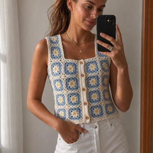 Könnte beinhalten: Ein ärmelloses Häkeloberteil mit quadratischem Ausschnitt und durchgehender Knopfleiste. Das Kleidungsstück besteht aus einzelnen Granny-Square-Motiven in den Farben Creme, Hellblau und Gelb und ist mit kleinen braunen Knöpfen versehen.