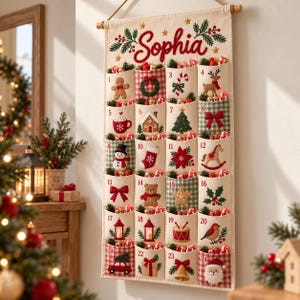 May include: A cream-colored fabric wall-hanging advent calendar with the name Sophia embroidered in red at the top. It features twenty-four numbered pockets, each decorated with embroidered Christmas motifs like gingerbread, reindeer, and Santa.