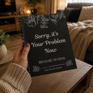 May include: A black spiral-bound notebook with the text "Sorry, it's Your Problem Now BECAUSE I'M DEAD" in white. Floral line art decorates the top and bottom. The notebook is held in a person's hand.