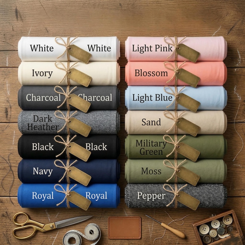 May include: A collection of rolled fabric bolts in various colors including white, ivory, charcoal, dark heather, black, navy, royal, light pink, blossom, light blue, sand, military green, moss, and pepper, each tied with twine and a blank tag.