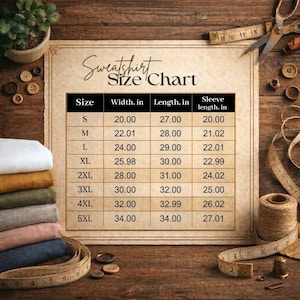 May include: A beige sweatshirt size chart printed on paper with black text, listing sizes S through 5XL with width, length, and sleeve length measurements in inches. The chart is surrounded by sewing supplies including buttons, fabric, and a measuring tape.