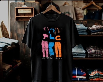 May include: A black short-sleeve t-shirt featuring a graphic print of three stylized figures in pink, blue, and orange pants. The letters T, L, and C are printed in matching colors above each figure, creating a vibrant design on the front of the shirt.