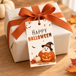 May include: A white gift box wrapped with a wide orange ribbon and bow, featuring a rectangular tag that reads Happy Halloween and From Christina, with an illustration of a ghost in a jack-o'-lantern, bats, and autumn leaves.
