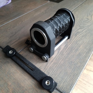 May include: A black bellows lens with a silver lens mount and a black focusing rail. The bellows has a pleated design. The lens is designed for macro photography. The item is on a wooden surface.