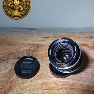 以下が含まれることがあります： HFTコーティングが施された黒いRollei Planar 1.8/50カメラレンズ。前面の縁にはシリアルナンバー1067580が印字されています。レンズには、分離した黒い円形のレンズキャップと、ユニットの底部に取り付けられた黒いリアレンズキャップが付属しています。