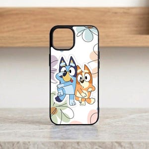 Pu&ograve; includere: Custodia per telefono nera con un'illustrazione a cartoni animati di due cani, uno blu e uno arancione, che si abbracciano. La custodia ha un bordo nero e uno sfondo bianco con motivi floreali pastello. La custodia &egrave; progettata per uno smartphone.