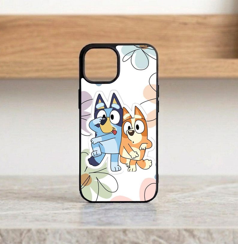 Pu&ograve; includere: Custodia per telefono nera con un'illustrazione a cartoni animati di due cani, uno blu e uno arancione, che si abbracciano. La custodia ha un bordo nero e uno sfondo bianco con motivi floreali pastello. La custodia &egrave; progettata per uno smartphone.
