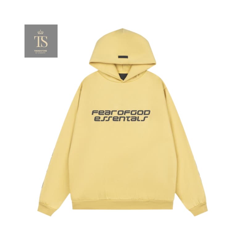 K&ouml;nnte beinhalten: Hellgelber Kapuzenpullover mit dem schwarzen Schriftzug "FEAR OF GOD essentials" auf der Brust. Der Kapuzenpullover hat eine Kapuze und ein kleines schwarzes Rechteck in der N&auml;he der Vorderseite der Kapuze. Die &Auml;rmel sind lang und das Material scheint weich zu sein.