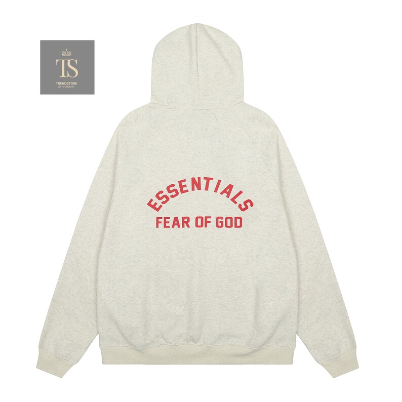 Op de afbeelding: Een lichtgrijs gem&ecirc;leerde hoodie met lange mouwen, een capuchon, geribbelde boorden en een geribbelde zoom. Op de achterkant staat de rode tekst ESSENTIALS in een boog boven de tekst FEAR OF GOD. Een klein vierkant logo met de letters TS is zichtbaar.