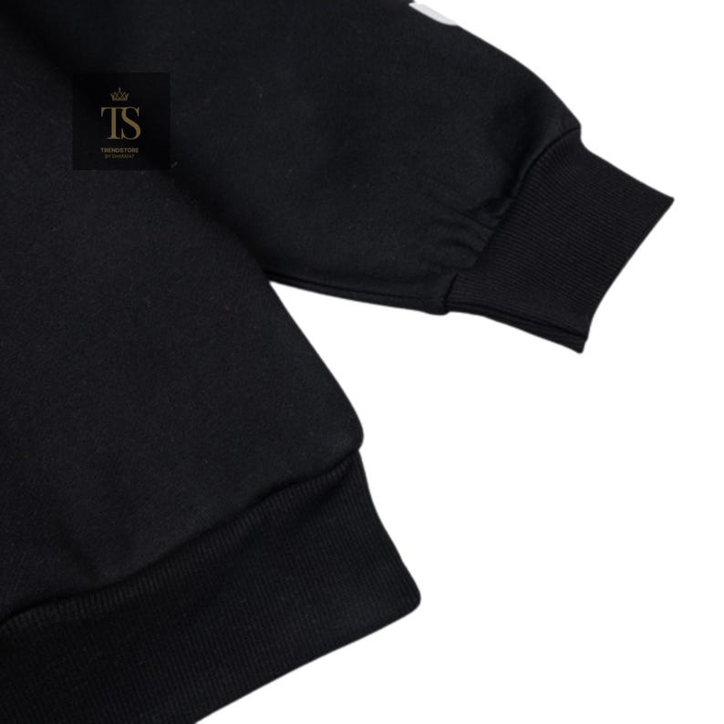 K&ouml;nnte beinhalten: Schwarzes Sweatshirt mit gerippten B&uuml;ndchen und Saum. Der &Auml;rmel hat ein wei&szlig;es Design am oberen Teil. Das Logo "TS TRENDSTORE" befindet sich in einem schwarzen Feld mit einer goldenen Krone.