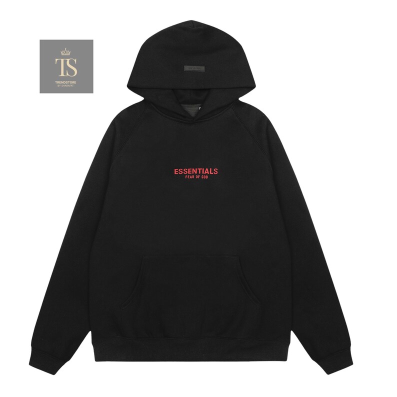 Op de afbeelding: Een zwarte hoodie met lange mouwen, een kangoeroezak aan de voorzijde en een capuchon. Op de borst staat de rode tekst ESSENTIALS FEAR OF GOD. Links bovenaan bevindt zich een klein vierkant logo met de letters TS en een kroonicoon.