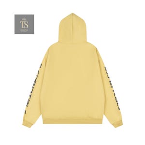 K&ouml;nnte beinhalten: Ein hellgelber Kapuzenpullover mit Kapuze und langen &Auml;rmeln. Die &Auml;rmel haben schwarzen Text. Die R&uuml;ckseite des Kapuzenpullovers ist schlicht. Der Kapuzenpullover ist aus einem weichen Material. Das Logo "TS TRENDSTORE" befindet sich in der oberen linken Ecke.