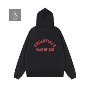 Może przedstawiać: Czarna bluza z kapturem i długimi rękawami. Z tyłu bluzy znajduje się czerwony napis "ESSENTIALS FEAR OF GOD" w łukowatym kształcie. Bluza wykonana jest z miękkiego materiału.