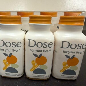May include: White bottles with orange caps are labeled "Dose for your liver." Each bottle has a graphic of an orange and ginger. The bottles are dietary supplements, each containing 2 fl oz (59 ml).