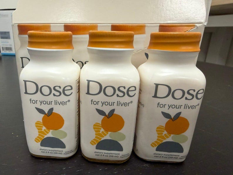 May include: White bottles with orange caps are labeled "Dose for your liver." Each bottle has a graphic of an orange and ginger. The bottles are dietary supplements, each containing 2 fl oz (59 ml).