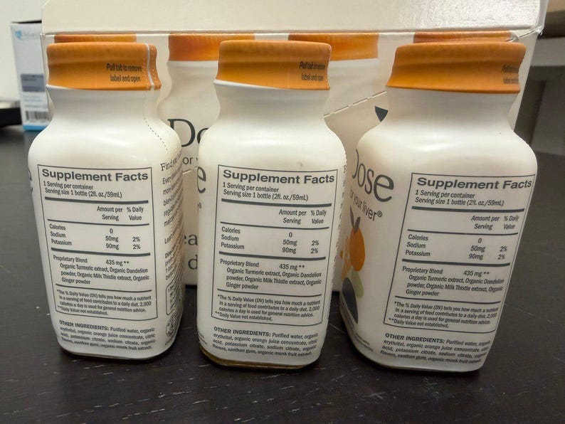 May include: White supplement bottles with orange caps are arranged in front of a box. Each bottle has a label with supplement facts, including calories, sodium, and potassium content. The bottles are filled with a liquid and are ready to drink.