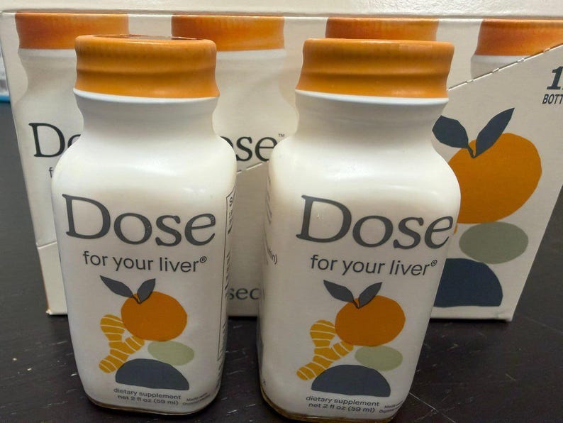May include: White bottles with orange caps and the text "Dose for your liver" are displayed. Each bottle has a graphic of an orange and ginger. The bottles are dietary supplements, each containing 2 fl oz (59 ml).